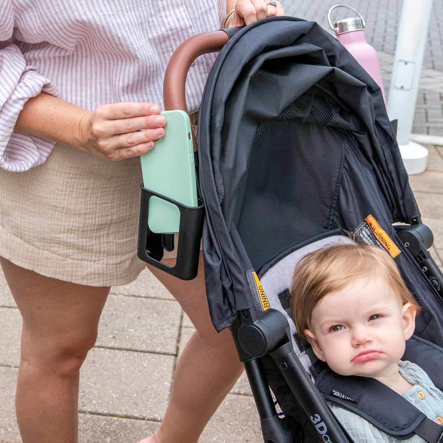 Demonstrates how the product can be used to conveniently hold a phone while using a stroller, showcasing its practical application for parents on-the-go.