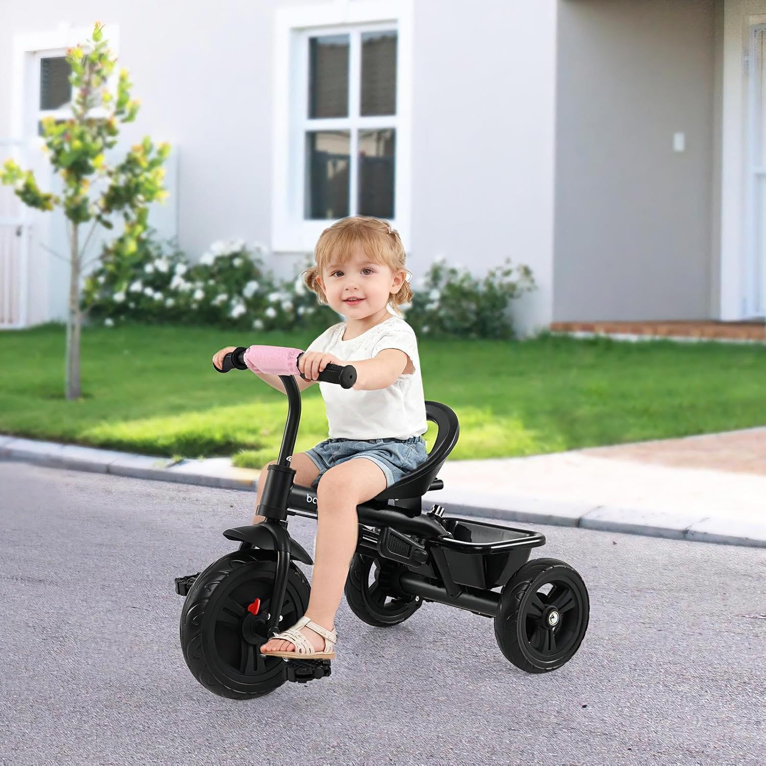 Shows a young child happily using the tricycle outdoors, demonstrating its suitability and appeal for toddlers.