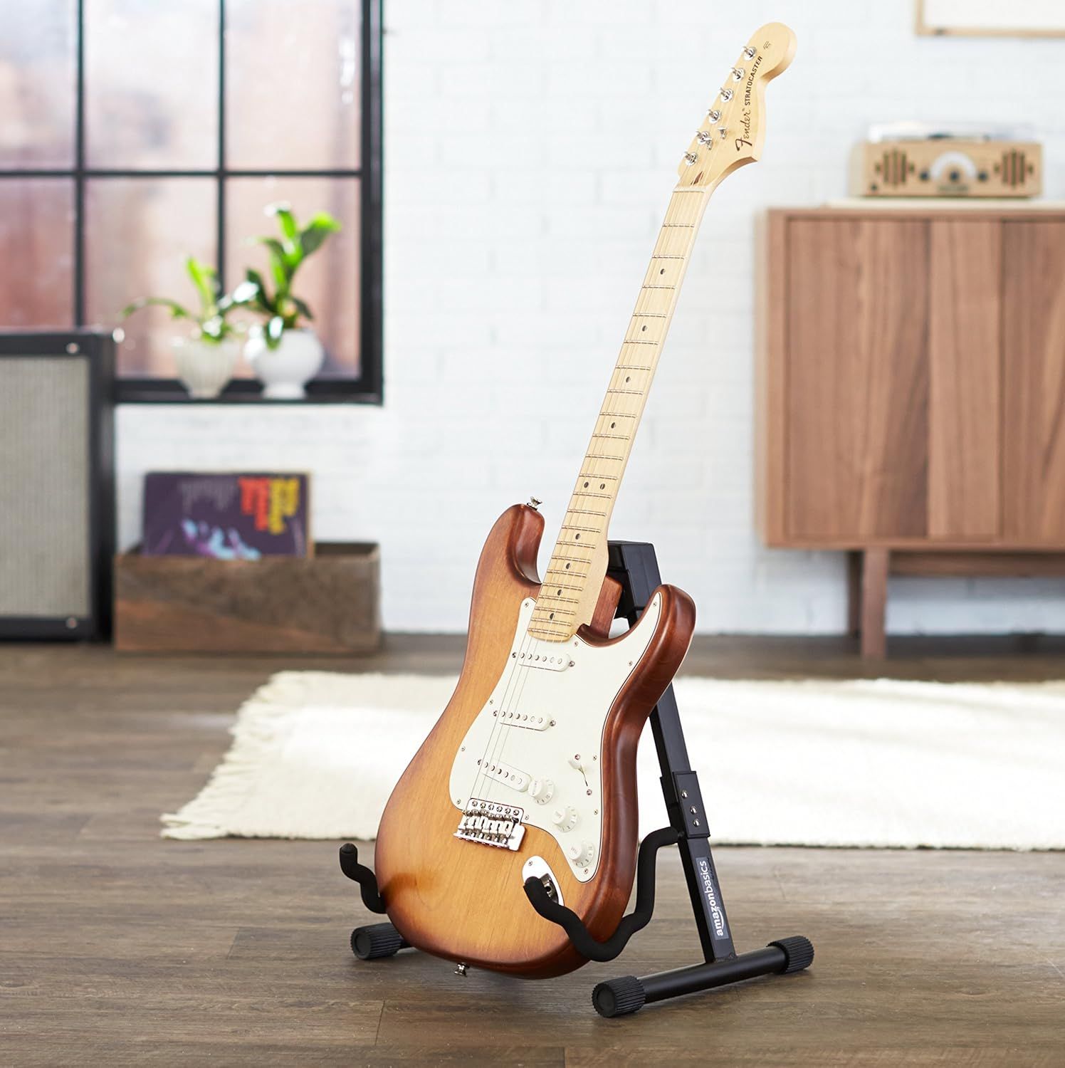 Shows the guitar displayed on a stand in a real-world home setting to help shoppers visualize how the product looks when not in use and fits into their living space.