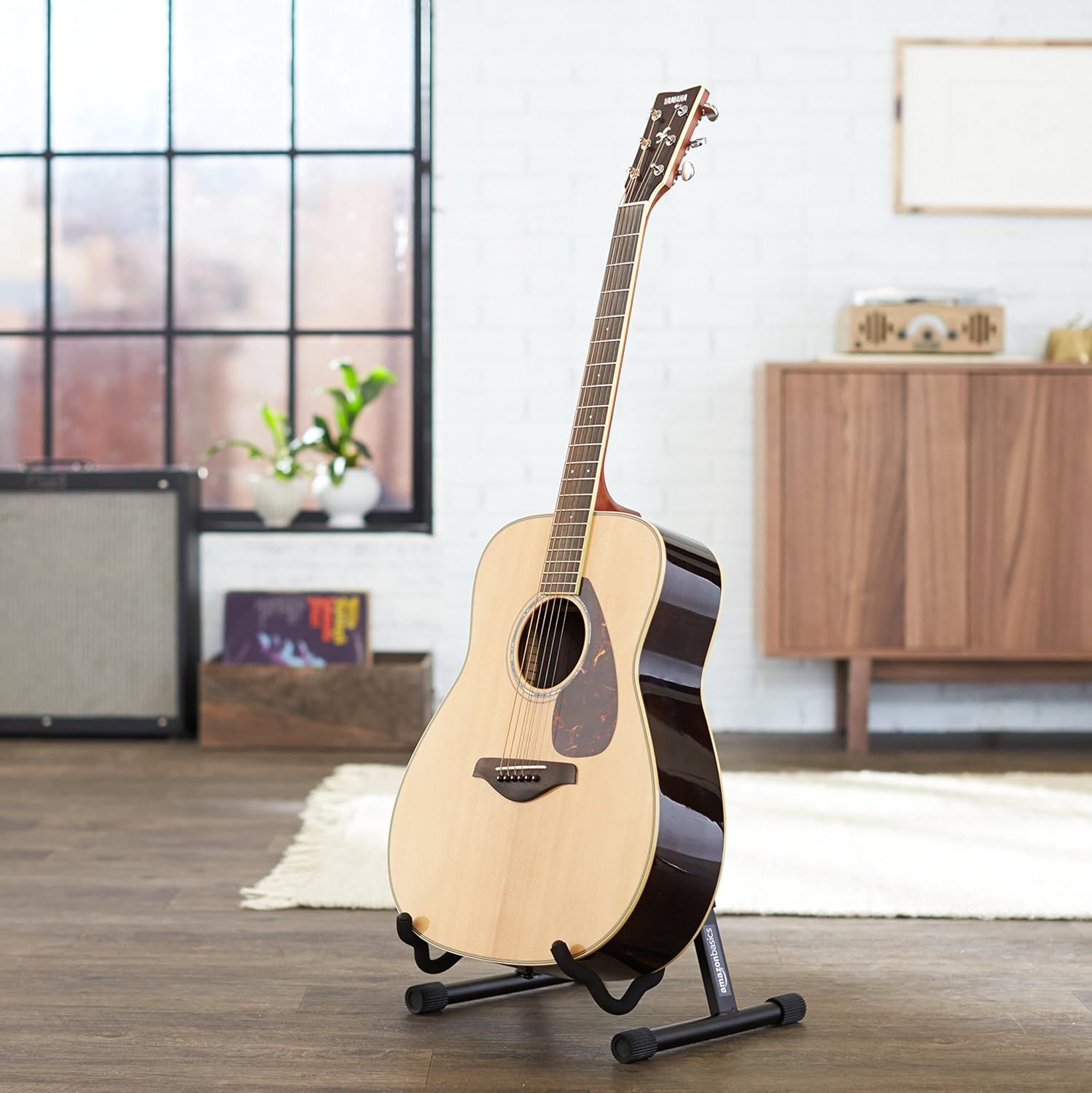 Shows the acoustic guitar displayed on a stand in a modern home setting to help shoppers visualize how the product looks in their own living space.
