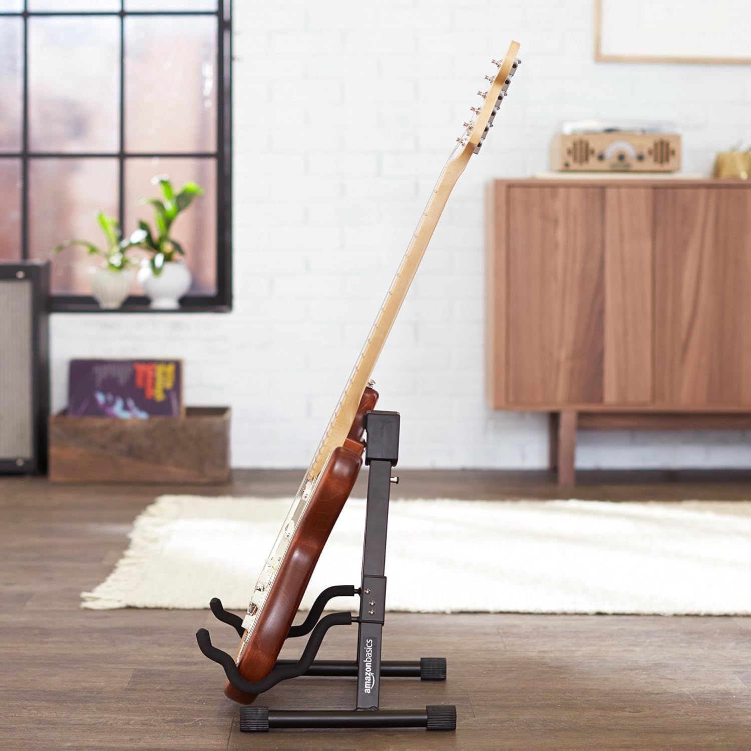 Shows the guitar stand holding a guitar in a real-world home setting to help shoppers visualize how the product looks and functions in their own space.