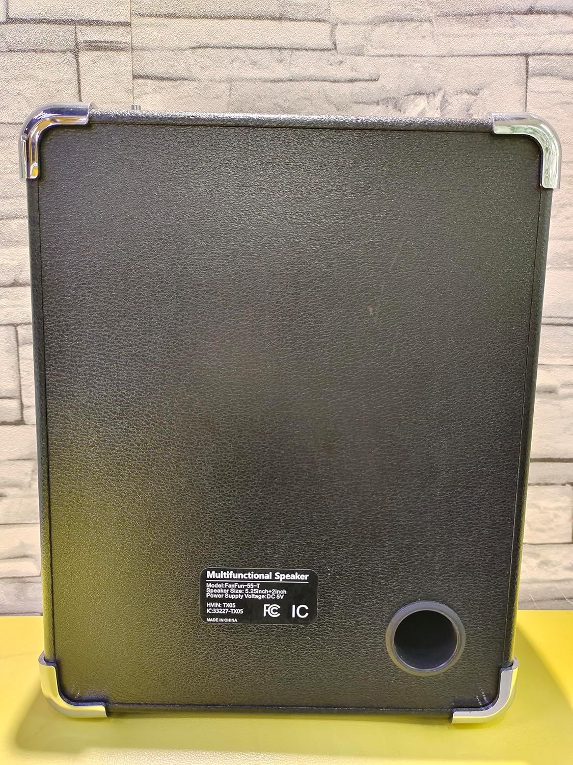 Shows the back view of the speaker to highlight structural components like the metal carrying handle, corner protectors, bass port, and product specifications label.