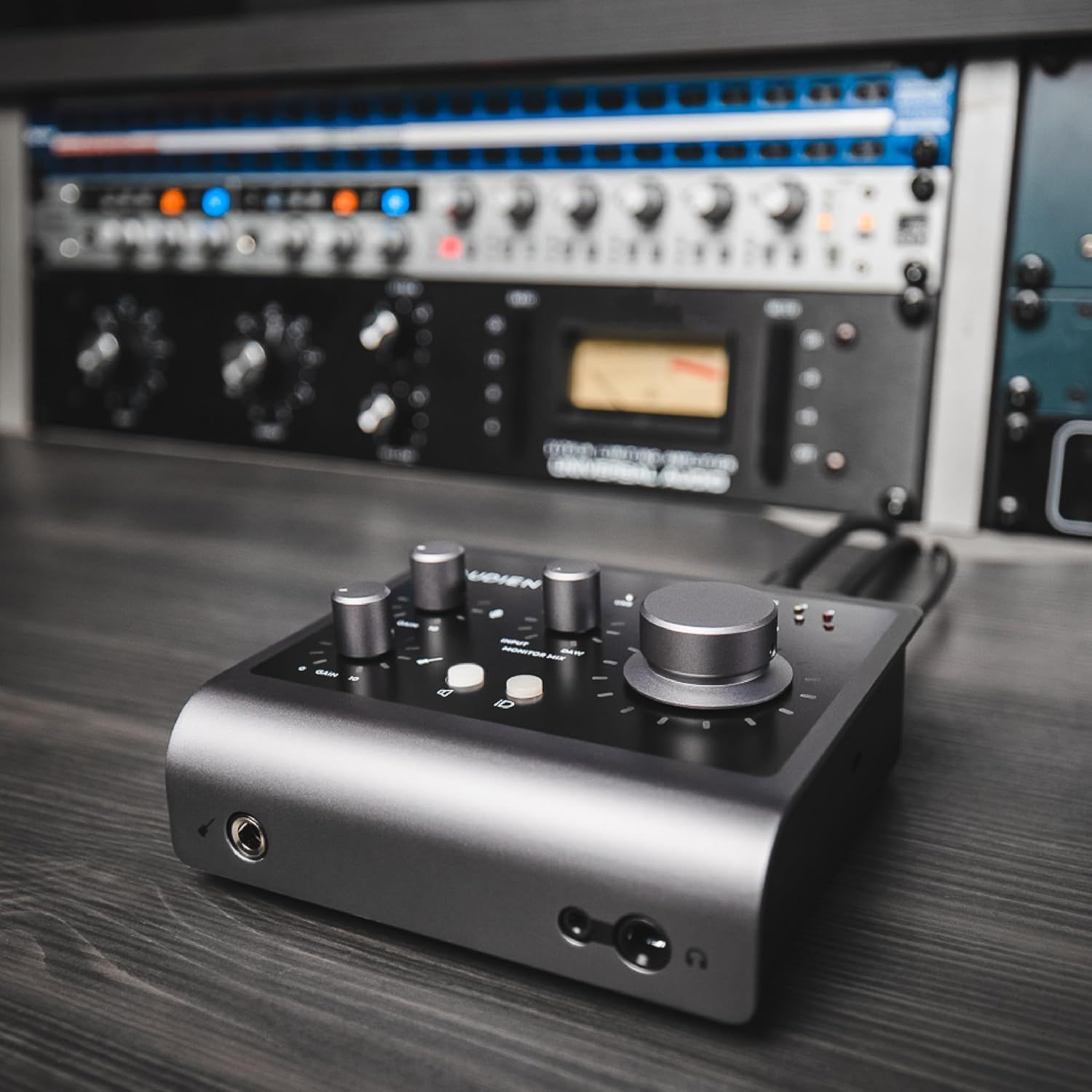 Shows the audio interface in a real-world professional studio setting with rack-mounted equipment in the background to demonstrate its intended use context and appeal to audio professionals.