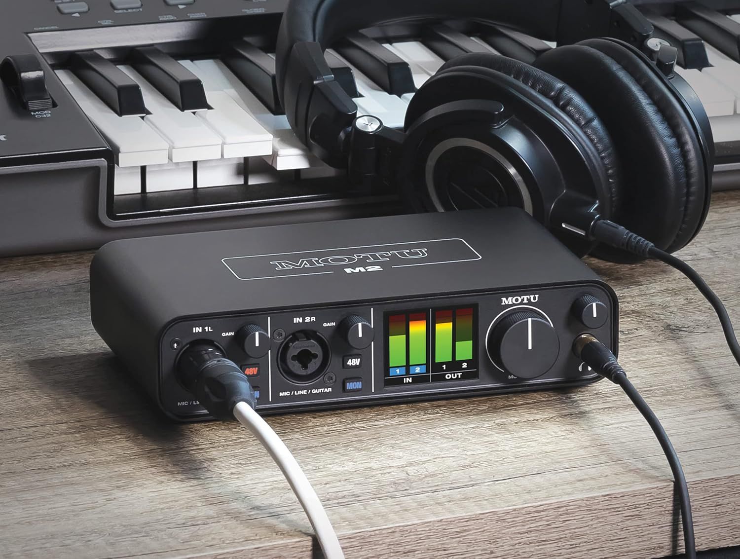 Shows the audio interface in a real-world music production environment with keyboard and headphones to help shoppers visualize how the product fits into their workflow.