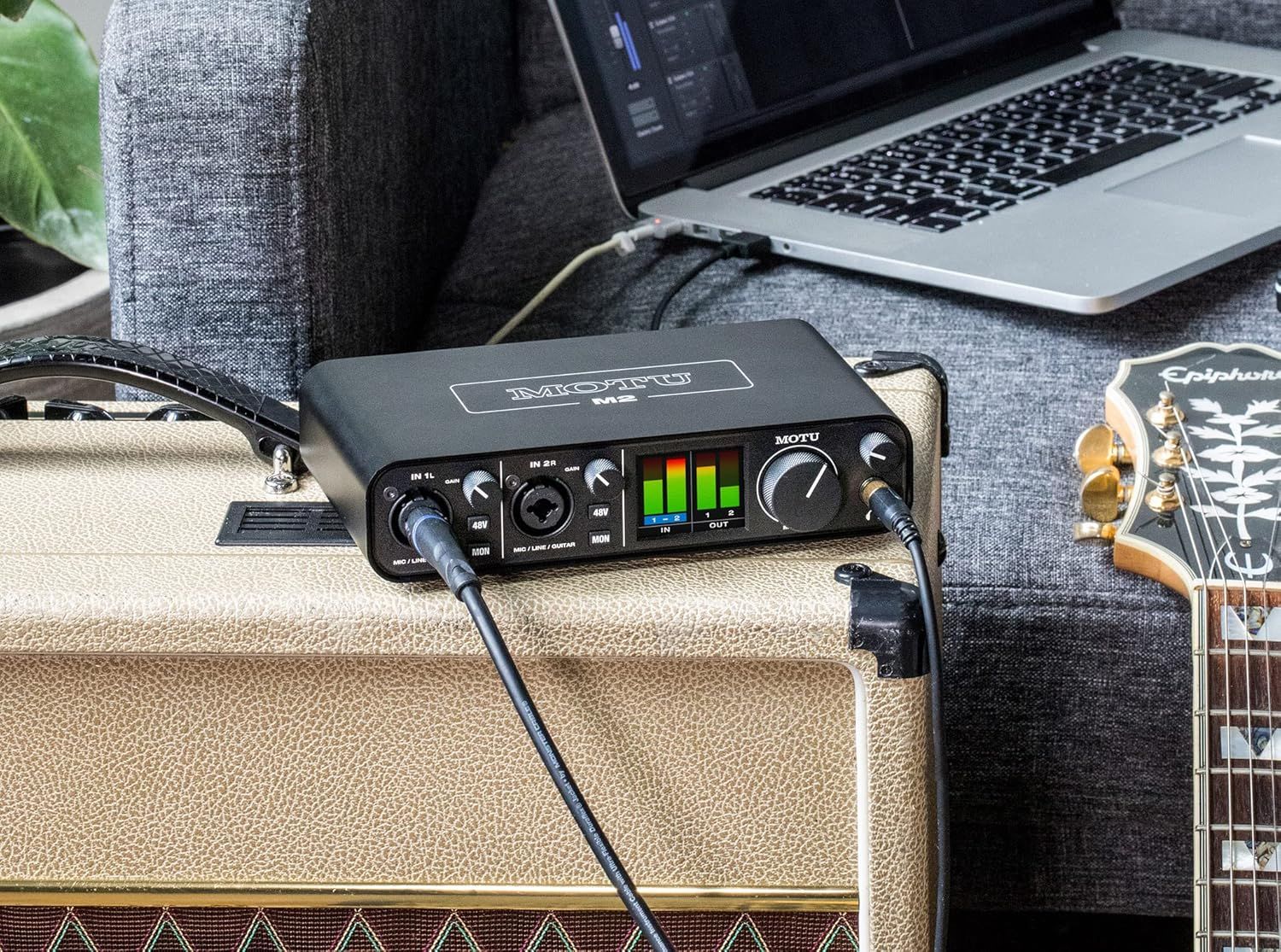 Shows the audio interface in an authentic home studio environment with guitar amp and laptop to help shoppers visualize how the product fits into their creative workflow.