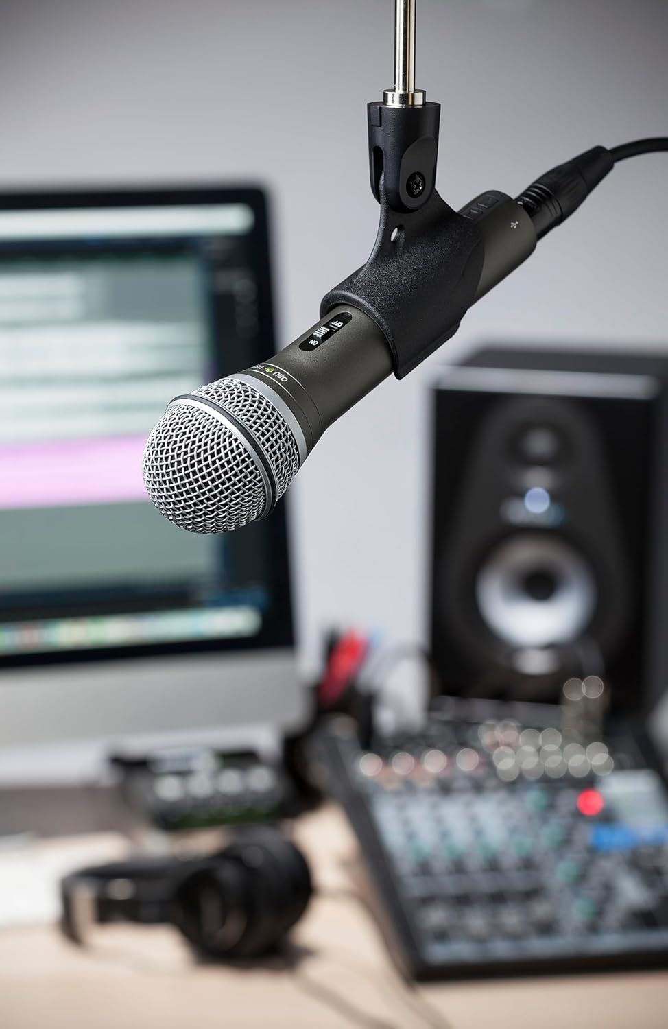 Shows the microphone in a real-world recording studio context with computer, speaker, and audio equipment to help shoppers visualize how the product fits into their workspace.
