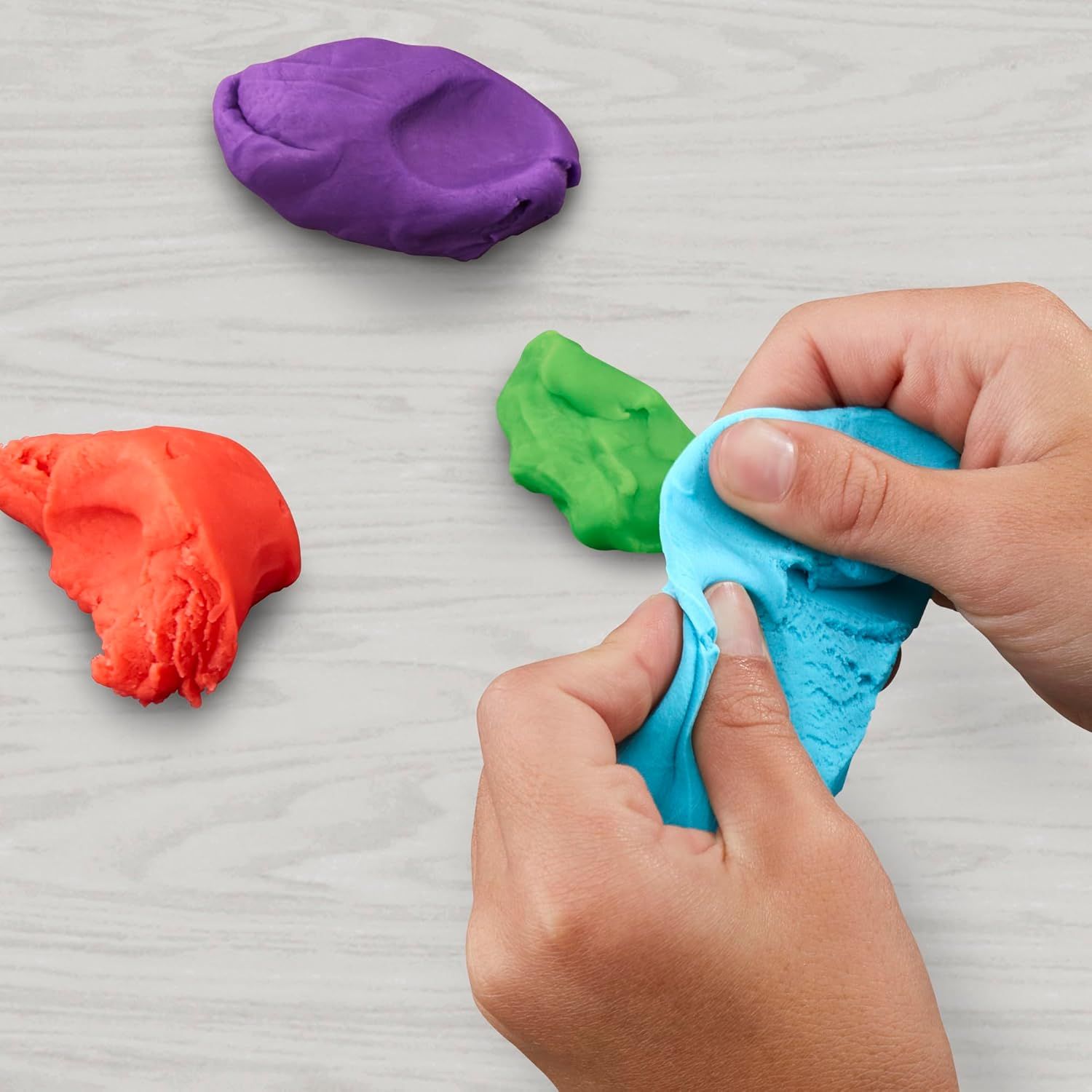 Demonstrates the product in use within a real-world play context, showing hands actively manipulating the colorful play dough to convey its tactile, sensory appeal.