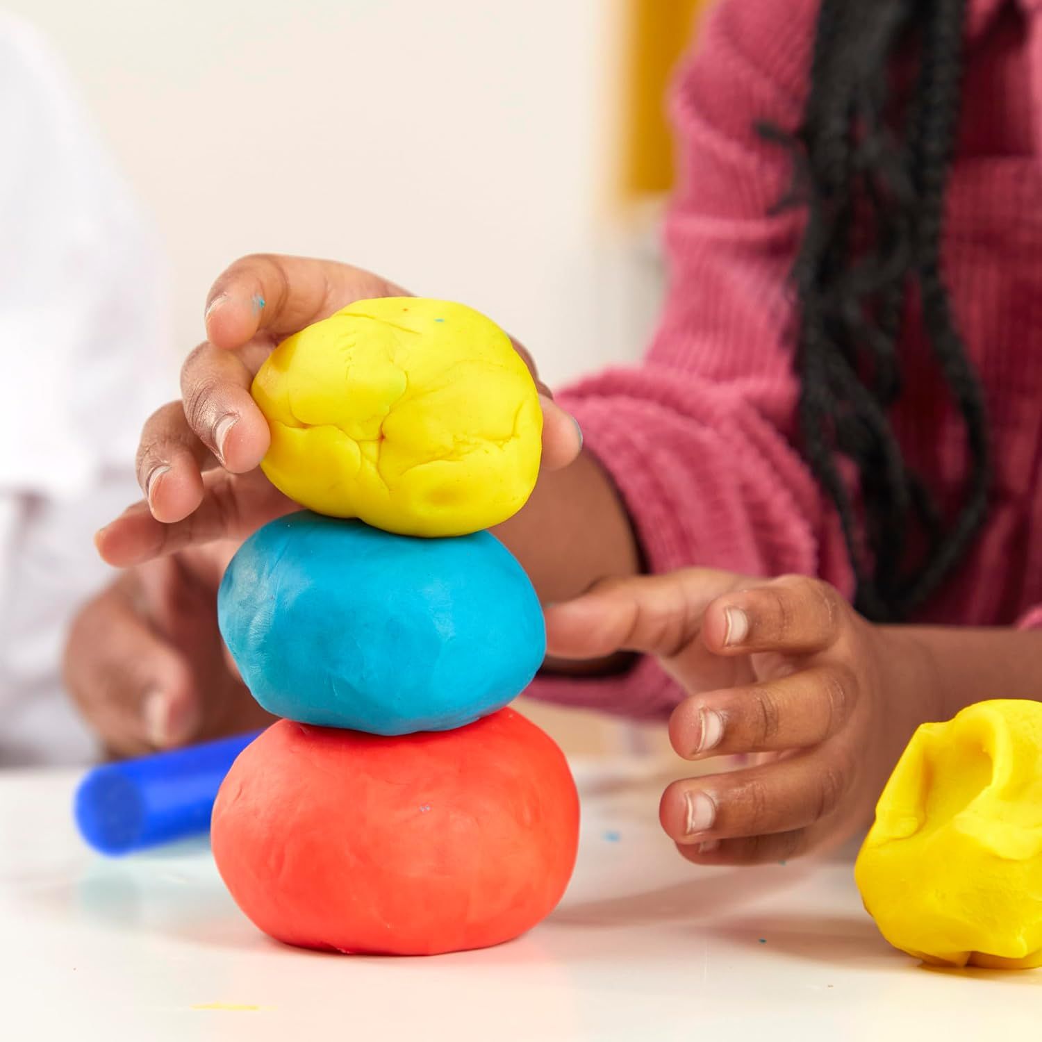 Shows the product in a real-world play context with a child actively using colorful play dough, helping shoppers visualize the product in use and its appeal to children.