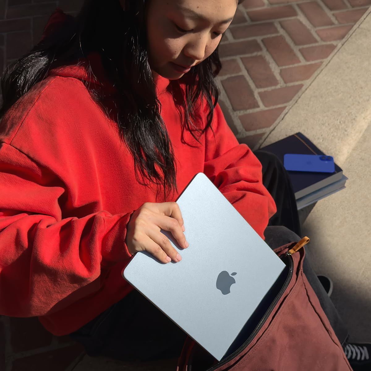 Demonstrates the product being used naturally in an everyday context (student with laptop and books) to help shoppers visualize the product in their own life.