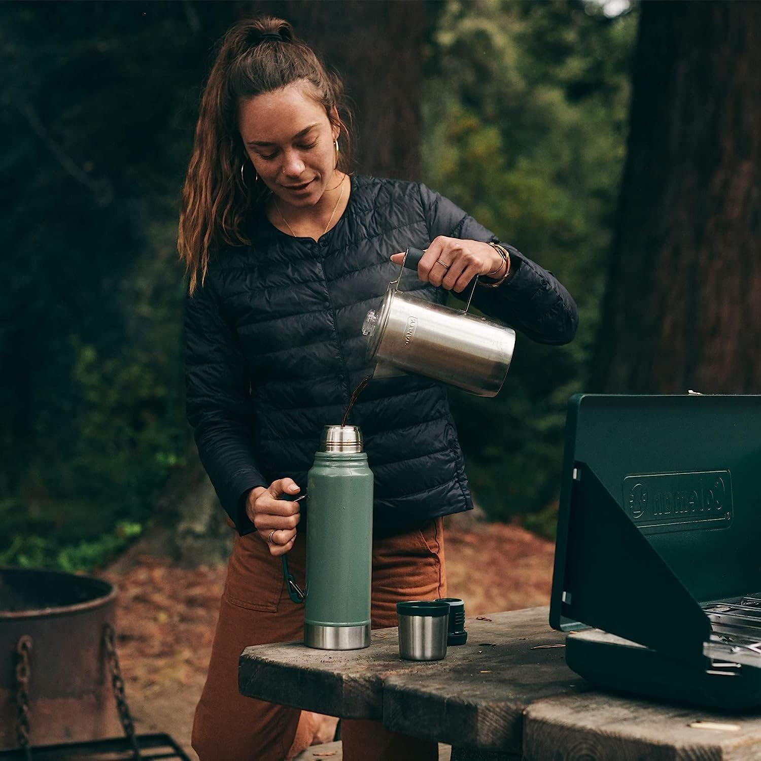 Demonstrates the product in a real-world outdoor camping context to help shoppers visualize using the thermos in nature settings.