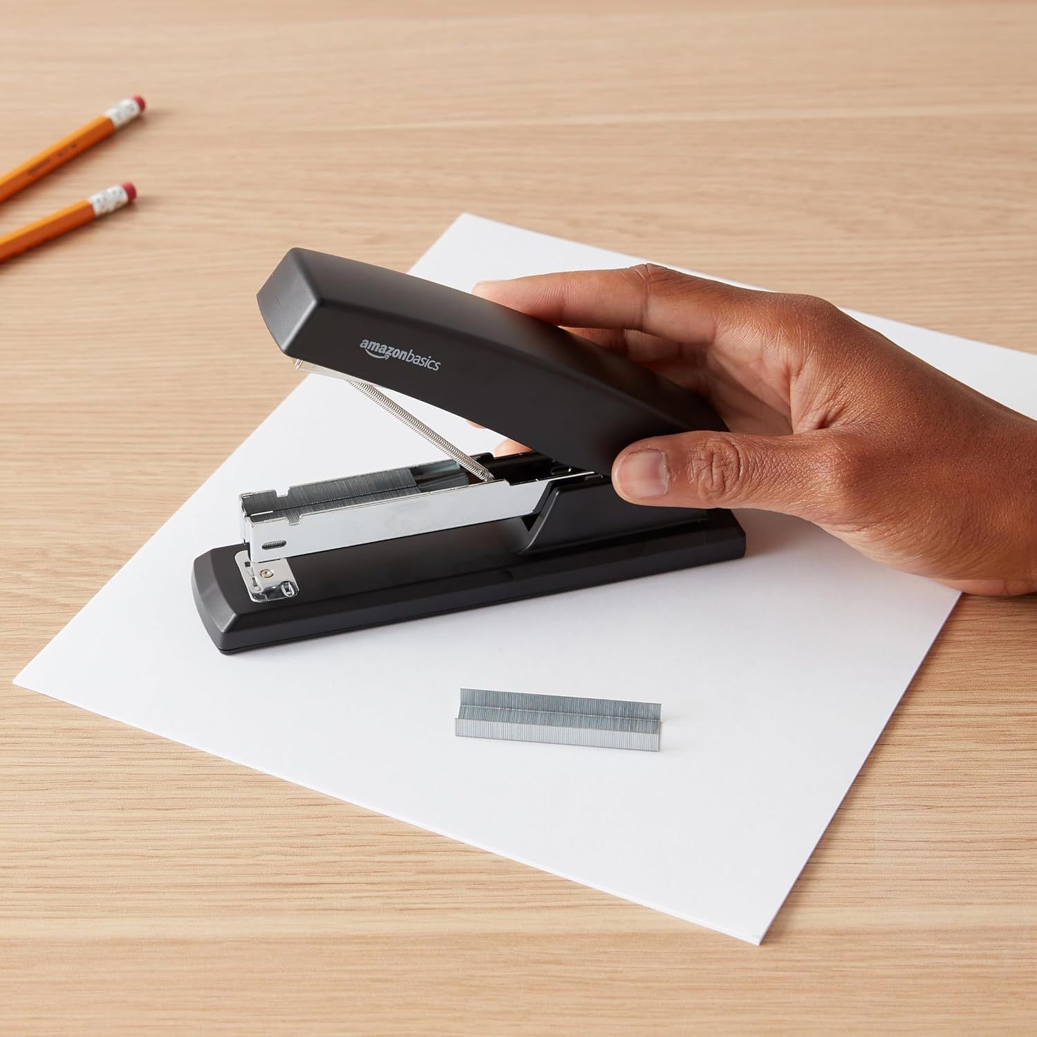 Shows the AmazonBasics stapler being used in a real office/desk environment to help shoppers visualize the product in everyday use.