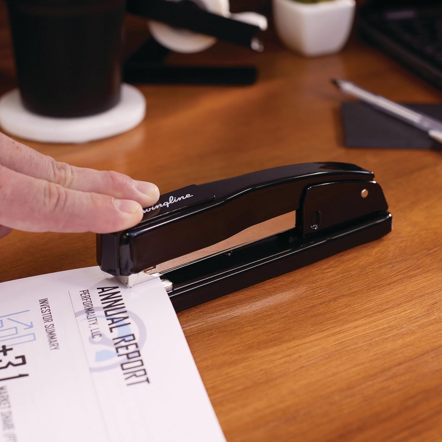 Demonstrates the product in a natural office/desk environment to help shoppers visualize how the stapler fits into everyday work scenarios.
