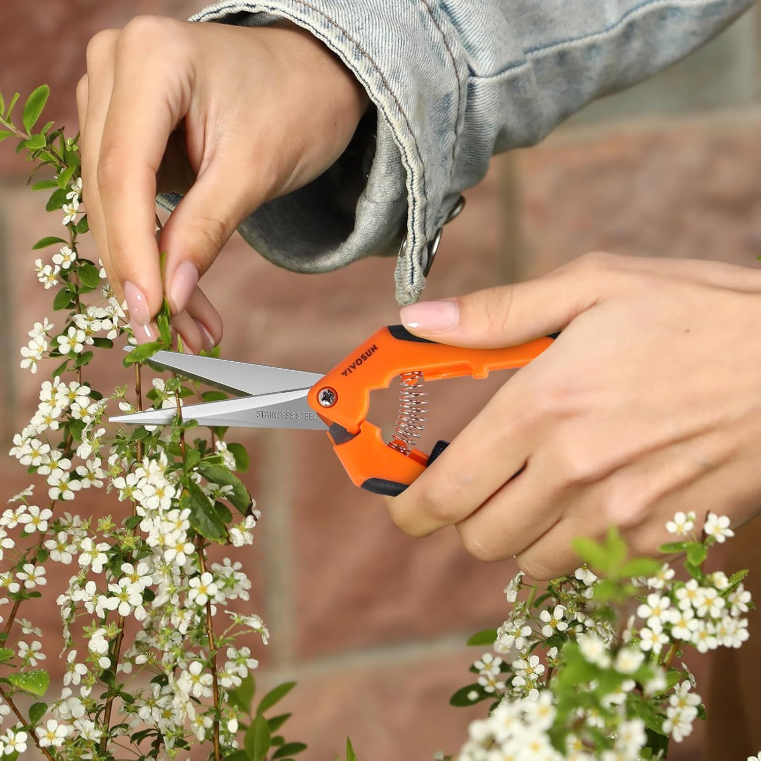 Demonstrates the product in a real-world gardening context, showing the pruning shears being used to trim flowering plants, helping shoppers visualize practical everyday use.
