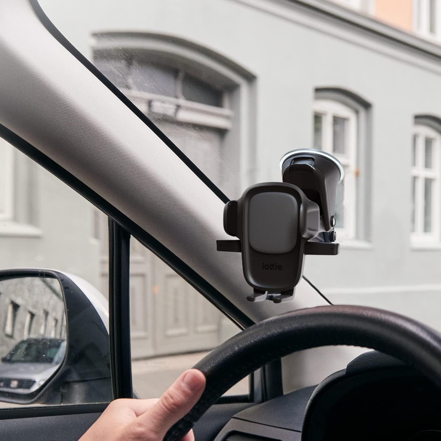 Demonstrates the product in a real-world driving context, showing how it mounts to the windshield for hands-free phone use while driving.