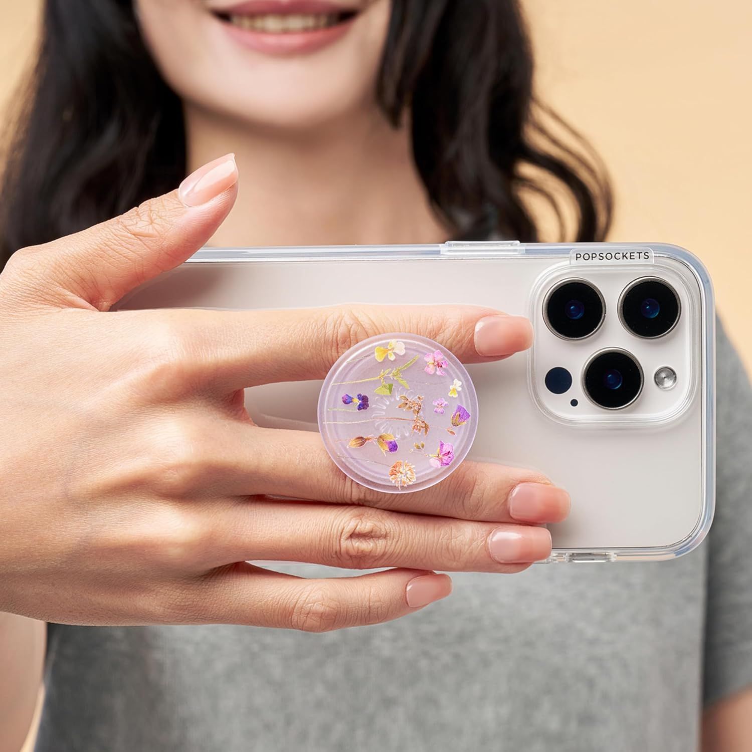 Demonstrates the product in real-world use, showing how the clear phone case and decorative PopSocket look when held by a user, helping shoppers visualize the product in everyday scenarios.