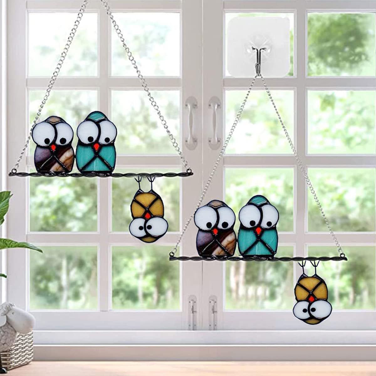 Shows the stained glass owl ornaments displayed in a real home window setting to help shoppers visualize how the product looks when hung and used as decorative window art.