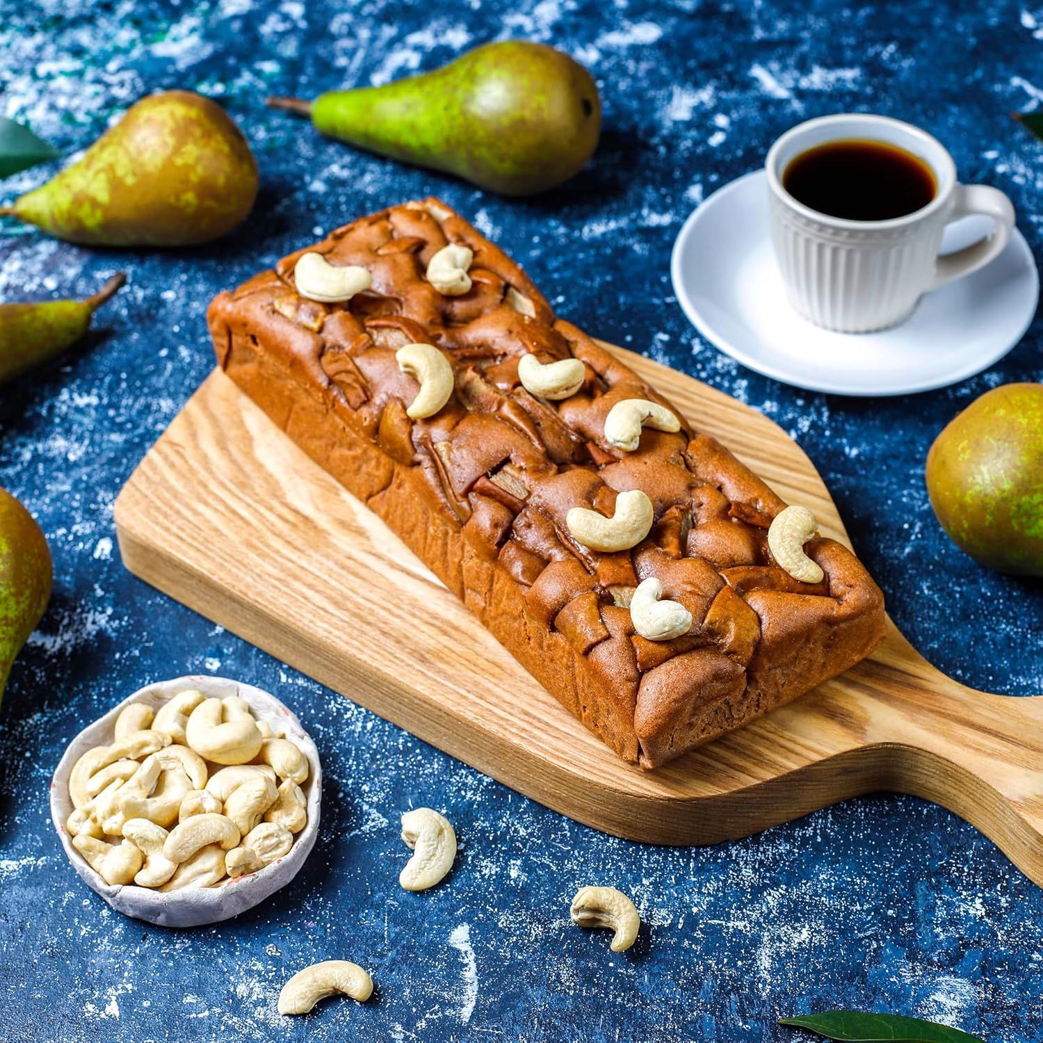 Showcases the product (loaf cake) in an appealing, aspirational lifestyle setting with complementary items like coffee, fresh pears, and cashews to evoke a premium, artisanal experience and inspire…