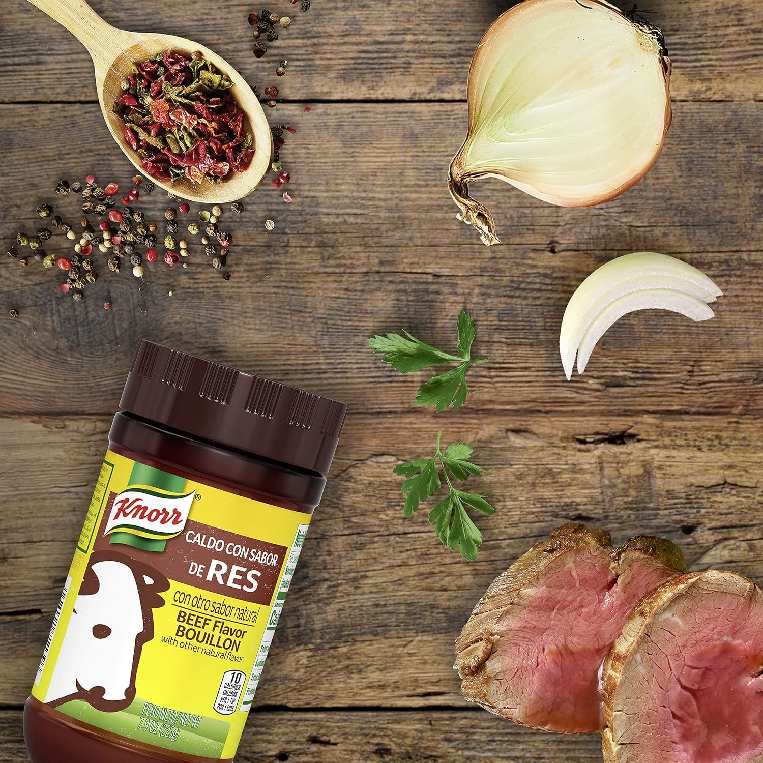 Shows the product alongside fresh ingredients (onion, peppercorns, herbs, cooked beef) to demonstrate what can be created with the bouillon, suggesting recipe versatility and inspiring culinary use.