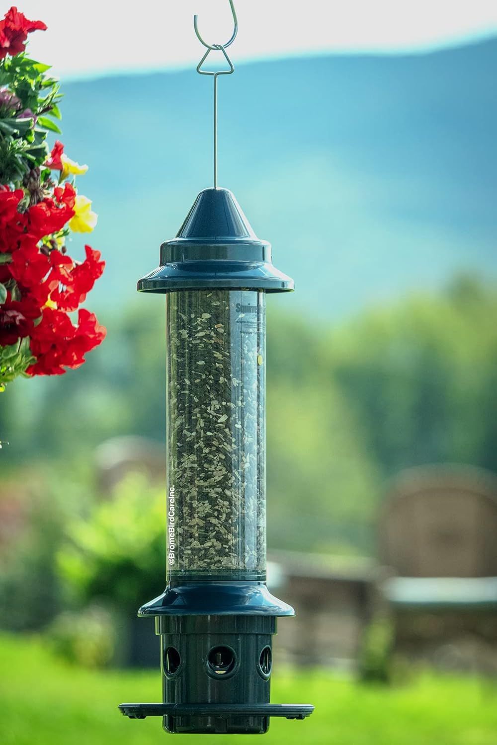 Showcases the bird feeder in a natural outdoor environment with flowers and greenery to help shoppers visualize how it will look in their own garden or yard.