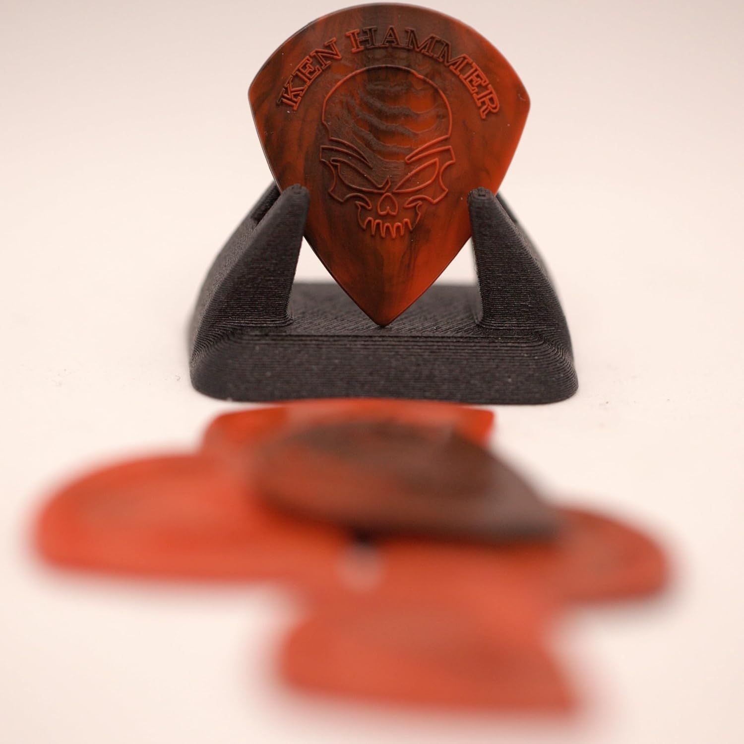 Shows the customer what is included in the purchase: a branded Ken Hammer guitar pick and a display stand for storage or presentation.
