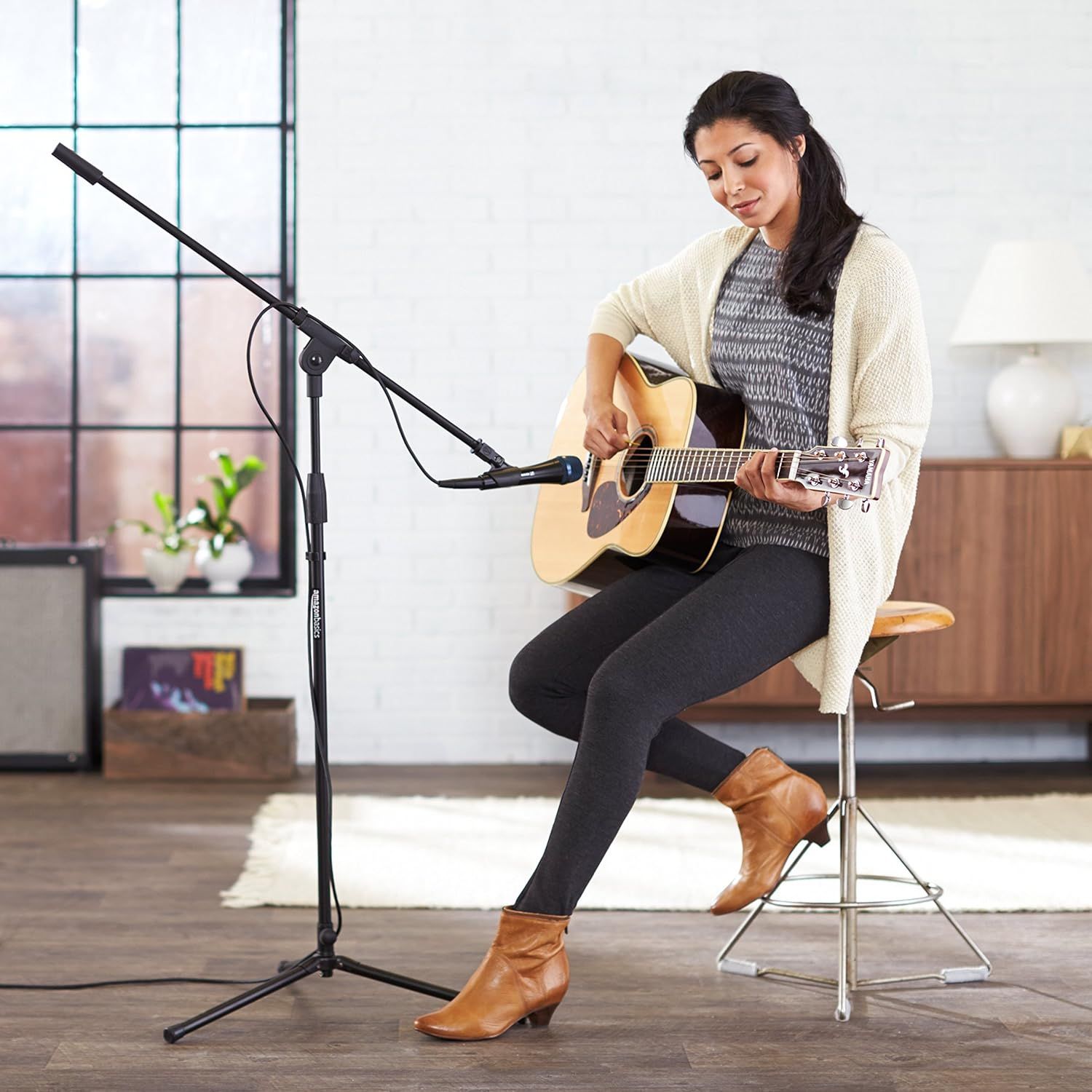 Shows the product (microphone stand) being used in a realistic home or studio environment to help shoppers visualize how it fits into their own space and usage scenarios.
