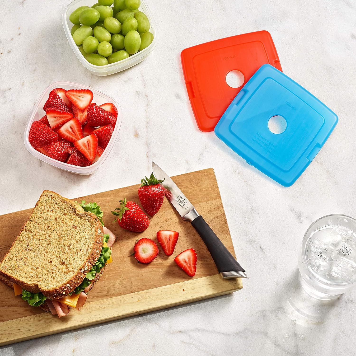 Demonstrates the product in a real-world meal prep context, showing the containers being used to store fresh fruits alongside a prepared lunch, helping shoppers visualize everyday use.