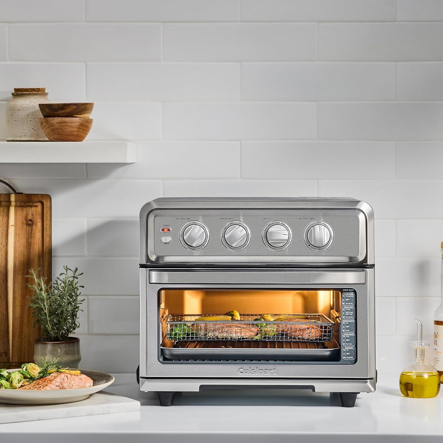 Shows the air fryer oven in a real kitchen setting with food being prepared, helping shoppers visualize how the product fits into their daily cooking routine.