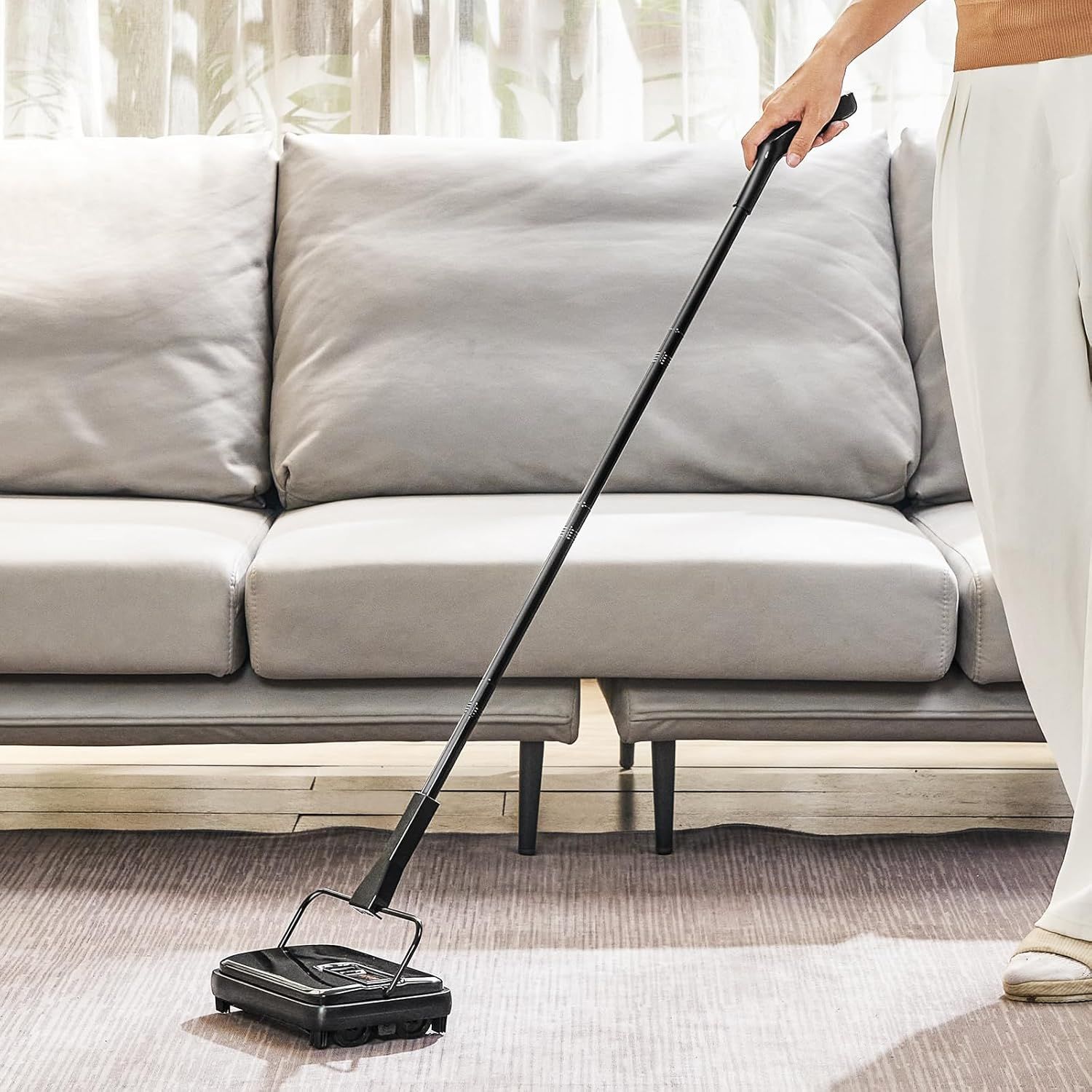 Demonstrates the product being used in a real-world home setting to help shoppers visualize how the manual carpet sweeper works on rugs and floors in their own living space.