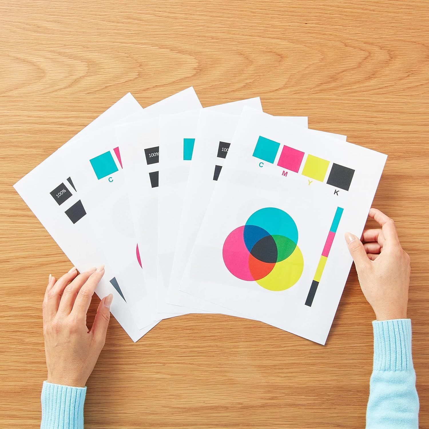 Shows the product in a natural, real-world setting with hands holding printed color calibration sheets to demonstrate actual use and output quality.