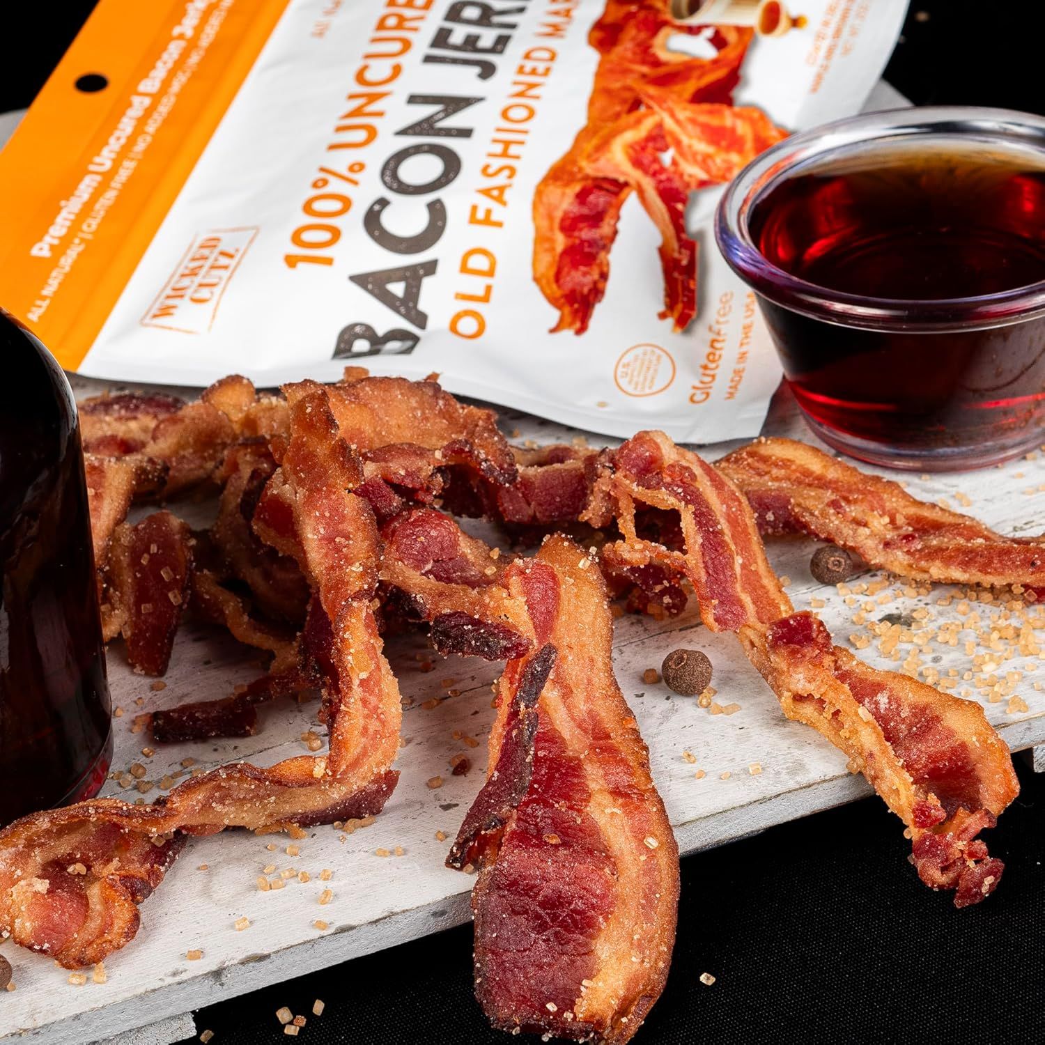 Showcases the bacon jerky product in an appetizing, real-world setting with complementary beverage to help shoppers visualize consumption and appeal.