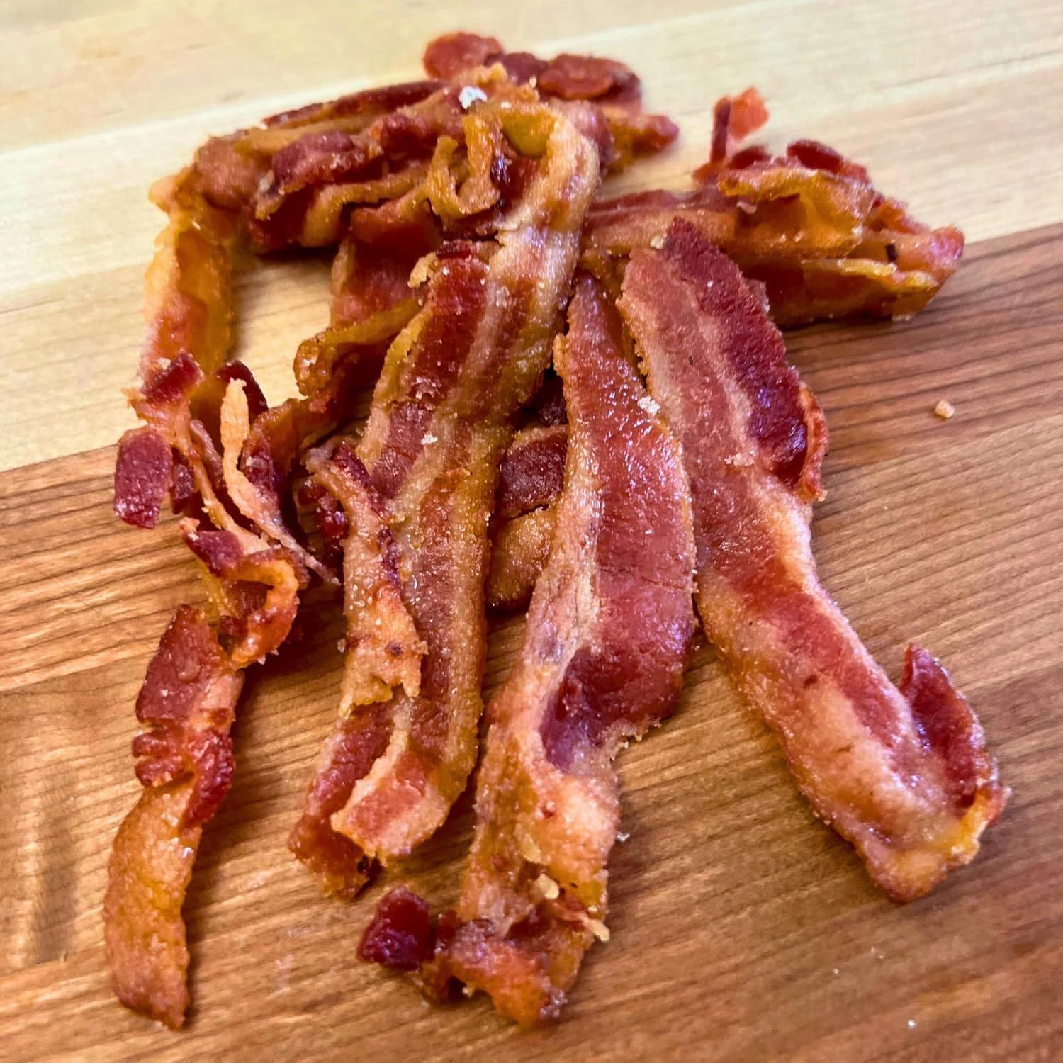 Shows the product (bacon) in a real-world context on a wooden cutting board to help shoppers visualize the cooked result and quality of the product.