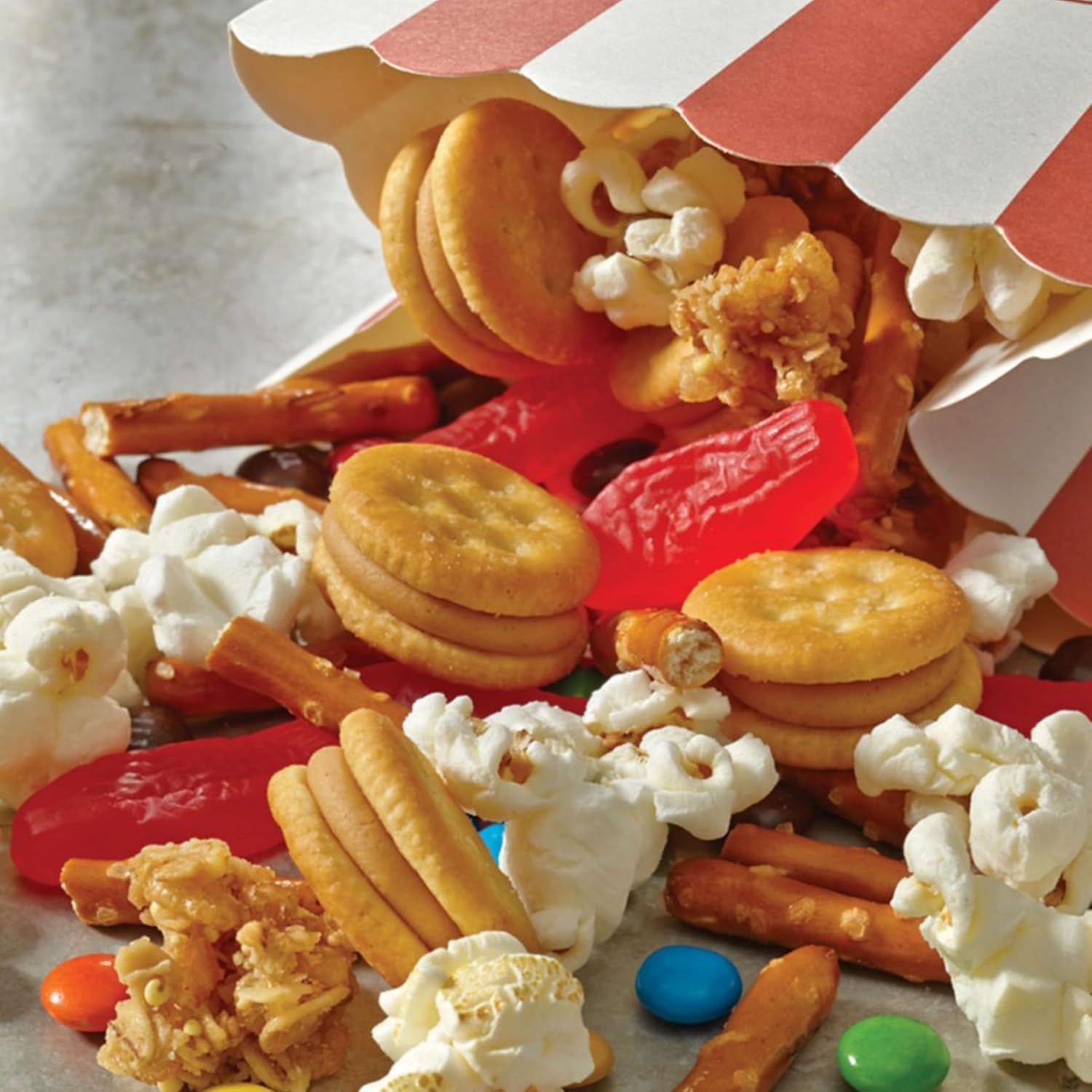 Shows all the different snack items included in the product—popcorn, pretzels, crackers, candy, and other treats—to communicate variety and value to the shopper.