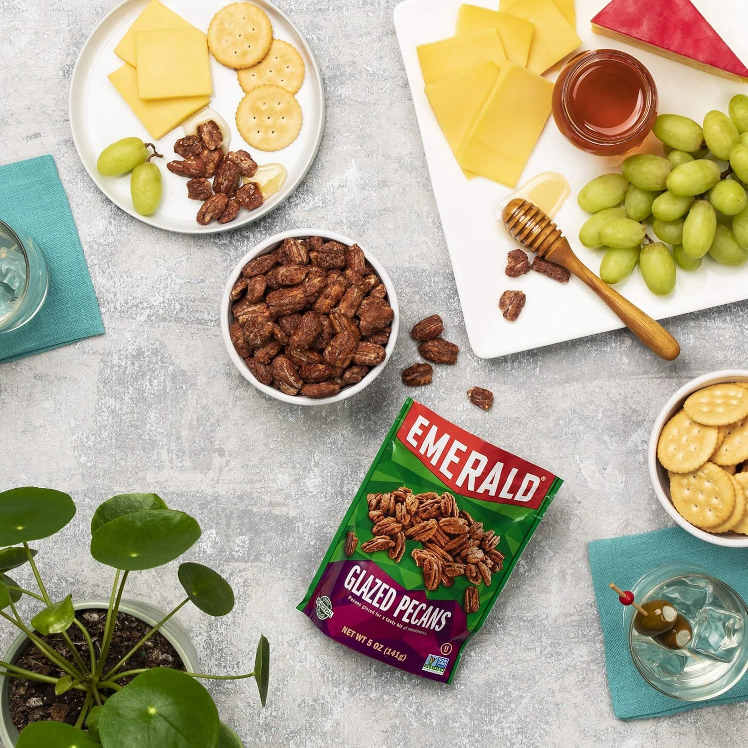 Showcases the product in a real-world entertaining context with complementary foods to help shoppers visualize how the glazed pecans fit into a charcuterie or snacking occasion.
