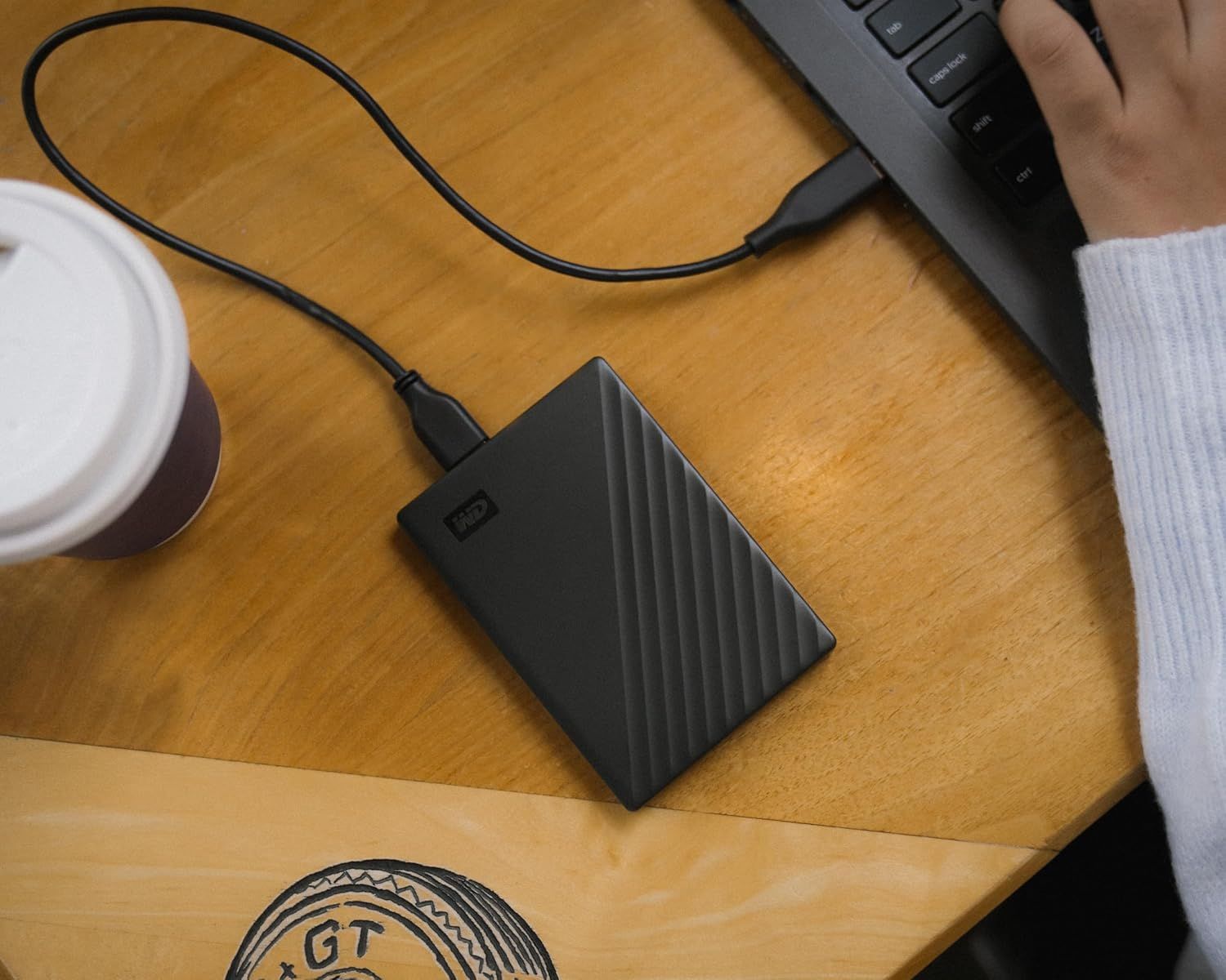 Demonstrates the product in a natural work environment to help shoppers visualize how the portable hard drive fits into their daily routine.