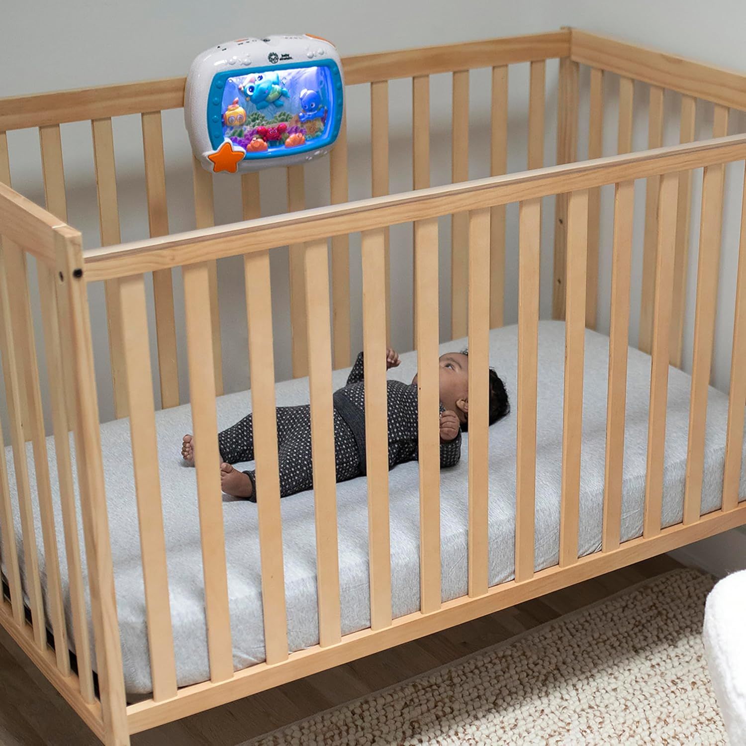 Demonstrates the product in a real-world nursery setting, showing a baby in a crib looking up at the attached toy to help shoppers visualize how it fits into their daily routine.