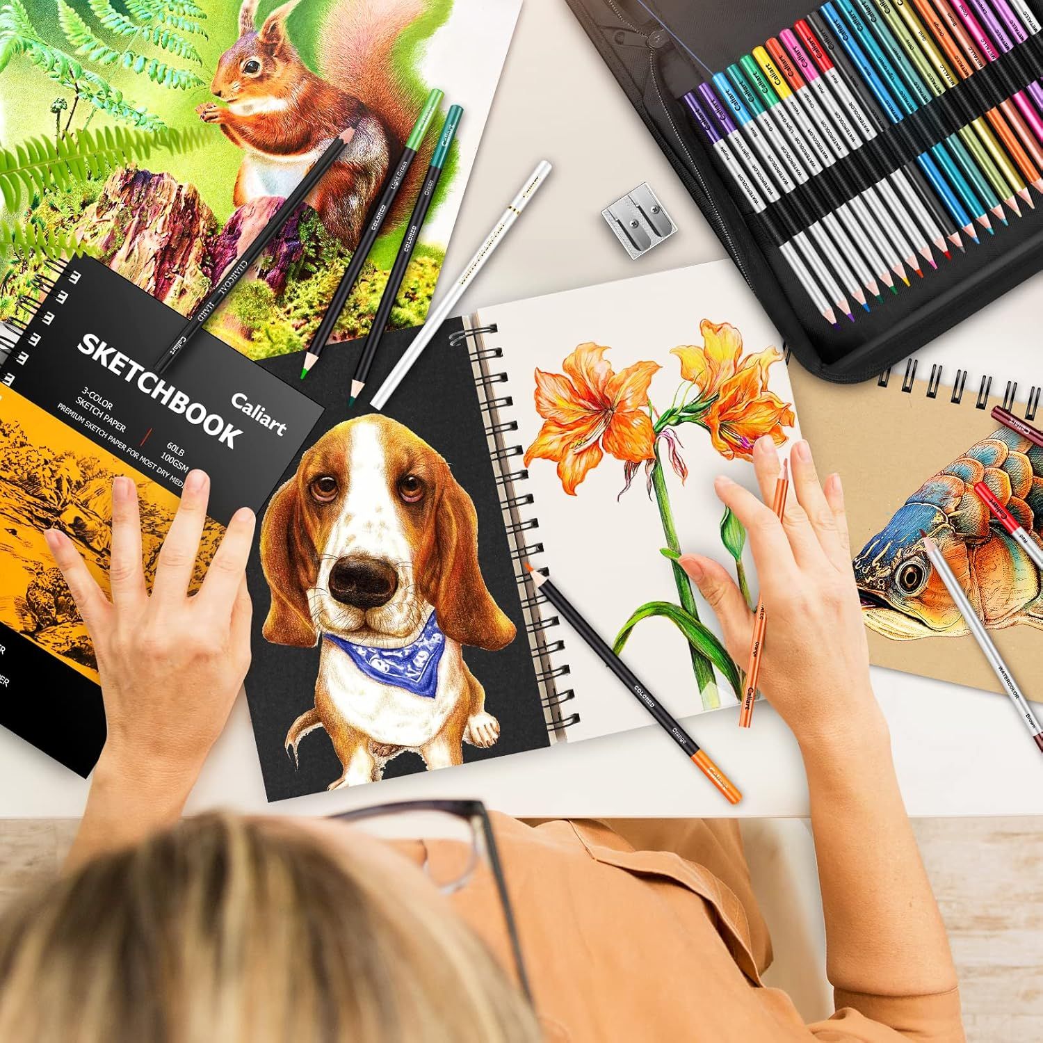 Shows everything included in the art set to help shoppers understand the complete bundle they will receive, including colored pencils, multiple sketchbooks with sample artwork, and accessories.