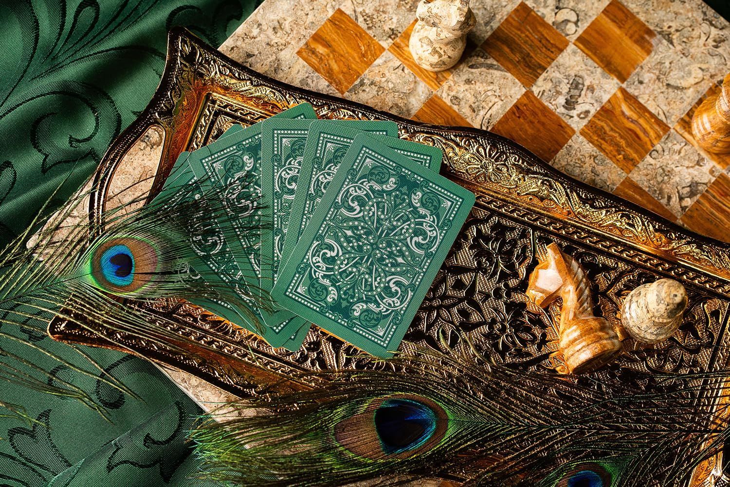 Displays the playing cards in an elegant lifestyle setting with ornate tray, peacock feathers, shells, and chess board to convey premium quality and sophisticated aesthetic appeal.
