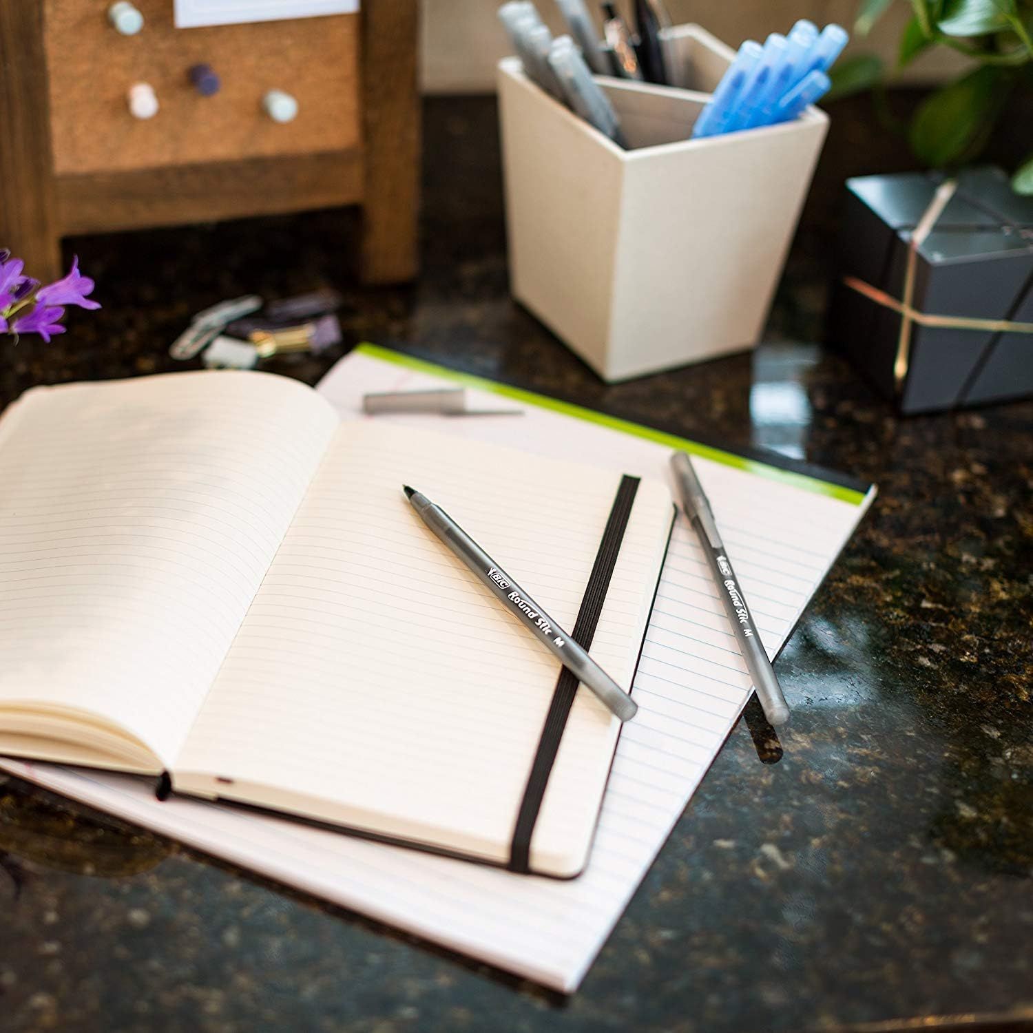 Showcases the product in a real-world home or office environment to help shoppers visualize how the notebooks and pens would fit into their daily workspace or lifestyle.