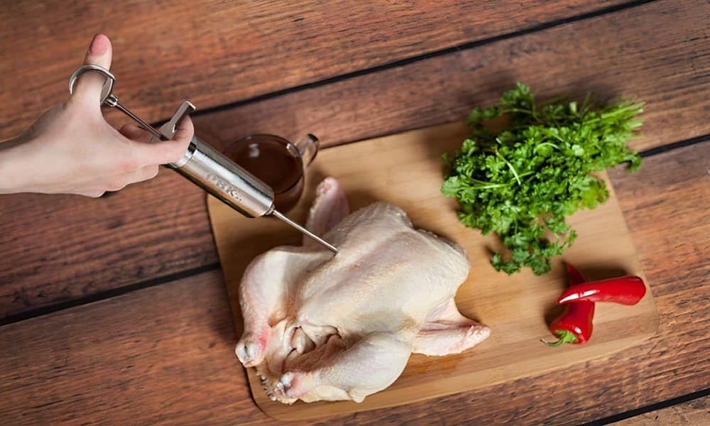 Demonstrates how to use the meat injector tool to inject marinade or seasoning into poultry, showing the proper technique for flavor enhancement.