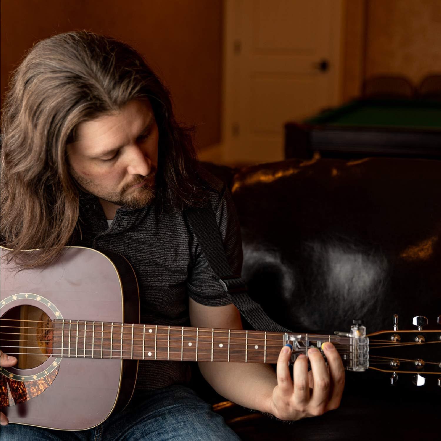 Shows the product in a real-world home setting with a guitarist using it naturally, helping shoppers visualize themselves using the ChordBuddy.