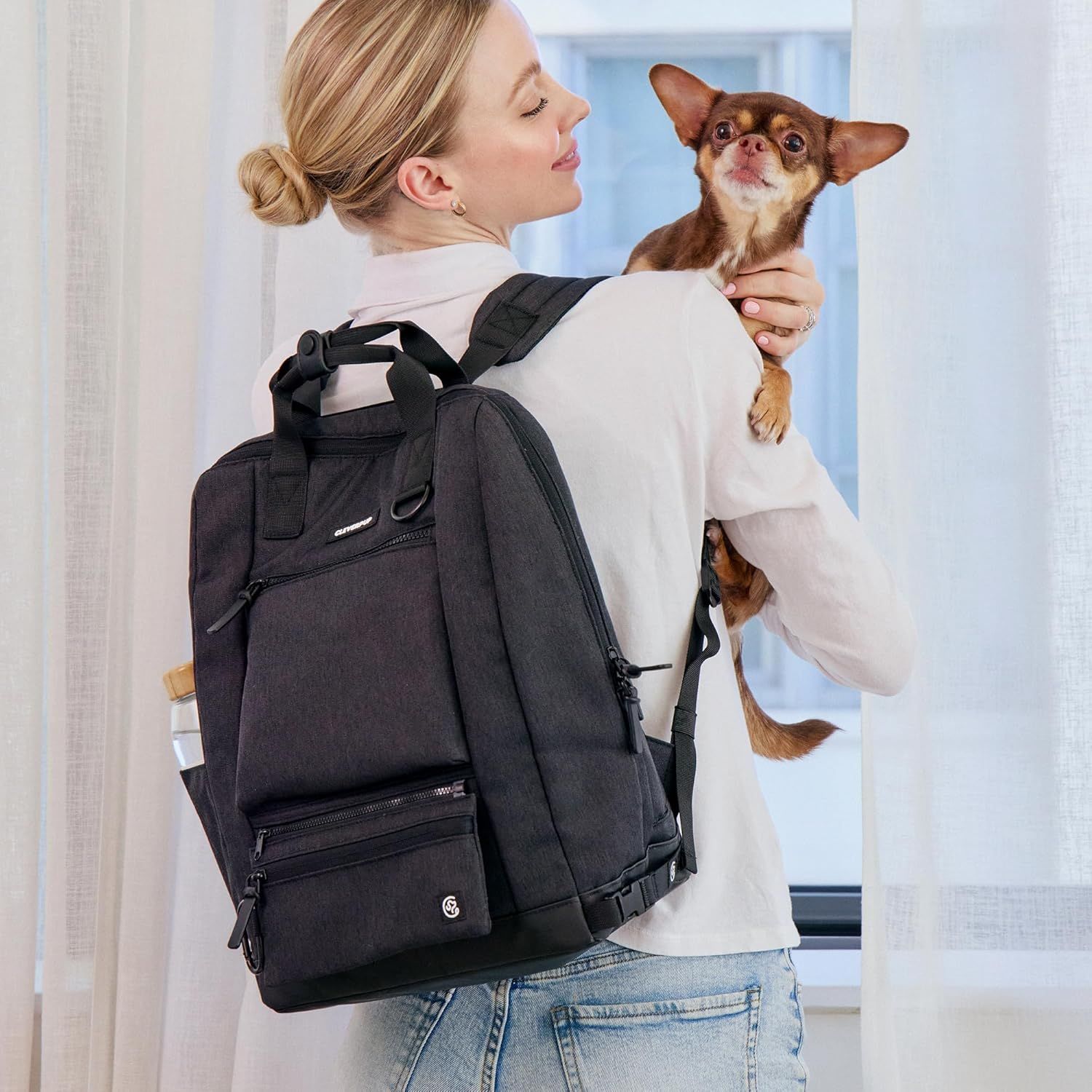 Shows the backpack being worn in a real-world home setting with a pet, demonstrating its practical use for pet owners.