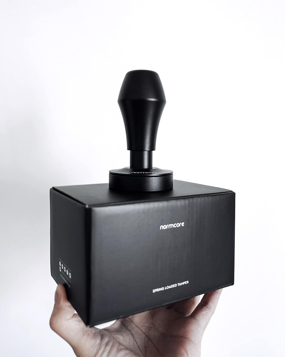 Highlights the spring-loaded tamper feature and compact portability of the product held in hand for scale reference.