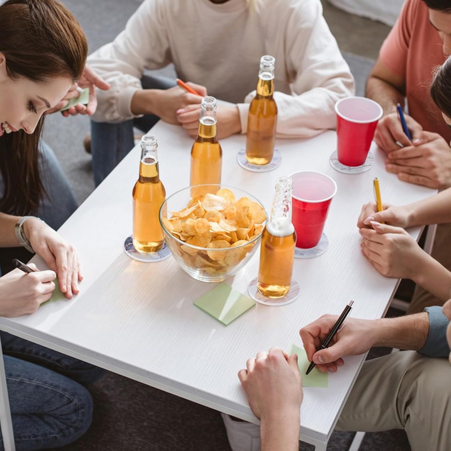 Shows the coasters being used in a social gathering context with multiple people and beverages to demonstrate the product's versatility for entertaining.